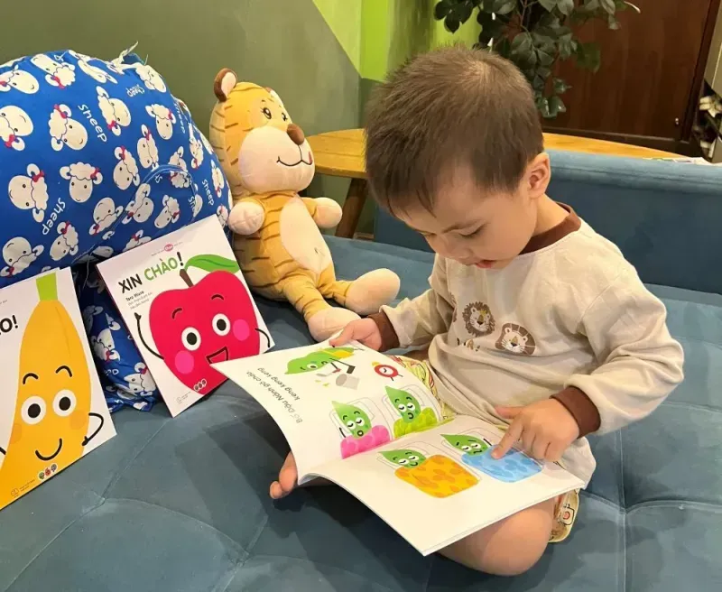 Một em bé đang tò mò lật mở một trang sách Ehon có hình vẽ chú thỏ khổng lồ với màu sắc tươi sáng, rực rỡ