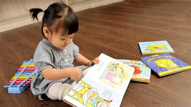 Bé 2 tuổi đang lật một cuốn sách tranh có hình các con vật ngộ nghĩnh, biểu cảm khuôn mặt thích thú khi nhận ra con chó và con mèo quen thuộc