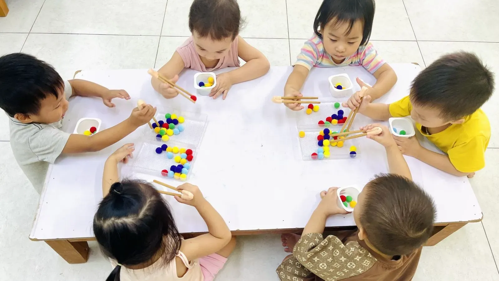 Bé đang chăm chú gắp các hạt pom pom bằng nhíp